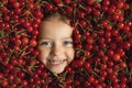 Face of a happy surrounded by a large pile of fruits of red, ripe, juicy cherries.