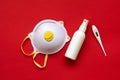 Face mask, bottle with hand sanitizer and thermometer on red background