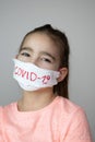 Girl with hand made face mask to protect her from Corona virus. COVID-19 written on mask. Royalty Free Stock Photo