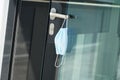 A face mask suspended on a door handle in a corporate building, close up. A reminder of safety measures in prevention of coronavir Royalty Free Stock Photo