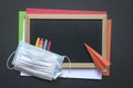 Face mask on top of crayons, black board and colored papers with paper plane Royalty Free Stock Photo