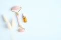 Face massage roller with jade stone with essential oil and dry flowers on blue background. Rose quartz facial massager, anti-aging Royalty Free Stock Photo