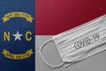 Face Medical Surgical White Mask with COVID-19 inscription lying on North Carolina Flag. Coronavirus in North Carolina