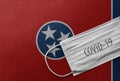 Face Medical Surgical White Mask with COVID-19 inscription lying on Tennessee State Flag. Coronavirus in Tennessee