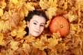 Face of teenage girl under maple leaves by pumpkin