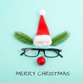 Face of a reindeer with a red bauble nose, fir antlers, a santa claus hat and eyeglasses, merry christmas greeting card