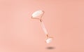 face roller made of rose quartz gua sha. hanging in the air on a beige background. flat lay. Royalty Free Stock Photo