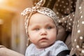 Face sad pensive emotional eight-month-old blue-eyes girl sitting in stroller looking away and wait for parent