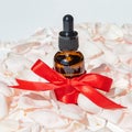 Face serum in a glass package, bottle on a pink rose petals background. treatment for skin with oils, vitamins and collagen. Royalty Free Stock Photo