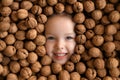 Face of a smiling girl is surrounded by a large pile of whole unpeeled walnuts