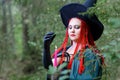 The face of the Sorceress with red hair in a pointed hat and a black cloak in the woods in the hand with a candle.