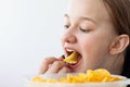 Face of a teenage girl close-up with her mouth open, her hand puts chips in her mouth, next to a large bowl of chips