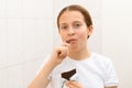 Face of a teenage girl with pimples, acne on the skin, she looks at herself in the mirror and eating a chocolate, concept of