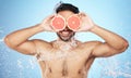 Face, water and grapefruit with a man model in studio on a blue background for hygiene or natural hydration. Skincare Royalty Free Stock Photo