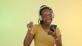 Face, woman and headphones on phone to dance, stream music and podcast by yellow background. Happy black person, excited