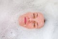 Face of a young beautiful girl in a white bath among soap bubbles from the foam bath gel, naked with wet hair, enjoys the spa trea Royalty Free Stock Photo