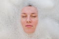 Face of a young beautiful girl in a white bath among soap bubbles from the foam bath gel, naked with wet hair, enjoys the spa trea Royalty Free Stock Photo