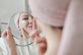 face of young beautiful healthy woman and reflection in the mirror. Young woman with a towel on head apply cream on face Royalty Free Stock Photo