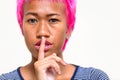 Face of young rebellious Asian woman with pink hair showing finger on lips