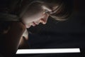 The face of a young woman lighted by a tablet screen light, the