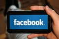 Facebook logo on the screen of a mobile phone in mans hand. Application for sharing photos, stories and blogging and