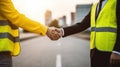 Faceless anonymous engineers in yellow waistcoat uniform shaking hands while standing on city street over blurred landscape with