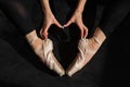 A faceless ballerina sits on the floor and makes a heart shape with her hands and pointe shoes. Top view.