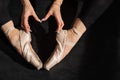A faceless ballerina sits on the floor and makes a heart shape with her hands and pointe shoes. Top view.