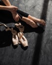 Faceless ballerina sits on the floor and puts on pointe shoes.