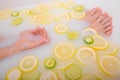 Faceless beautiful young woman takes a bath with milk lemons and lime. Cropped photo. Close-up of female hands and feet Royalty Free Stock Photo