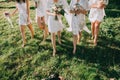 Faceless bridesmaids and bride in satin robes with bouquets in hands walk barefoot on the grass. Royalty Free Stock Photo