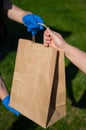 Faceless courier in gloves hands an eco friendly old lady`s paper bag in the park. The concept of order delivery