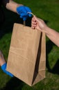 Faceless courier in gloves hands an eco friendly old lady`s paper bag in the park. The concept of order delivery