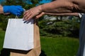 A faceless courier in gloves hands an eco friendly paper bag to a customer in a park. The concept of donation of