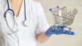 A faceless doctor with a medical coat and a stethoscope holds a small shopping cart full of medicines. Pharmacy concept.