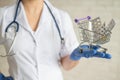 A faceless doctor with a medical coat and a stethoscope holds a small shopping cart full of medicines. Pharmacy concept.