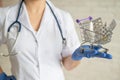 A faceless doctor with a medical coat and a stethoscope holds a small shopping cart full of medicines. Pharmacy concept.