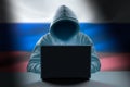 Faceless hooded anonymous russian hacker on Russian flag background. Anonymous person in hood sitting in front of computer working
