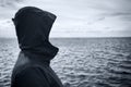 Faceless hooded person looking at horizon over sea water