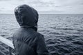 Faceless hooded person looking at horizon over sea water