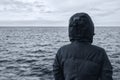 Faceless hooded person looking at horizon over sea water