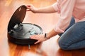 Faceless middle section of young woman cleaning the deposit of an automatic vacuum cleaner to clean the floor, opened machine hous