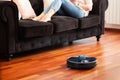 Faceless middle section of young woman relaxing on coach using automatic vacuum cleaner to clean the floor