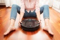 Faceless middle section of young woman seated at floor holding an intelligent vacuum cleaner to clean the floor