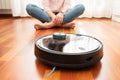 Faceless middle section of young woman seated at floor while using automatic vacuum cleaner to clean the floor