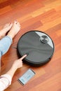 Faceless middle section of young woman touching an automatic vacuum cleaner to clean the floor, controlling smart machine housewor