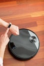 Faceless middle section of young woman touching an smart watch to control an automatic vacuum cleaner to clean the floor