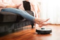 Faceless middle section of young woman using automatic vacuum cleaner to clean the floor, controlling smart housework robo