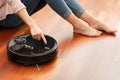 Faceless middle section of young woman using automatic vacuum cleaner to clean the floor, controlling smart machine housework robo