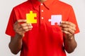 Faceless person wearing red casual style T-shirt, holding two puzzle parts, connecting colorful jigsaw pieces, symbol of unity and